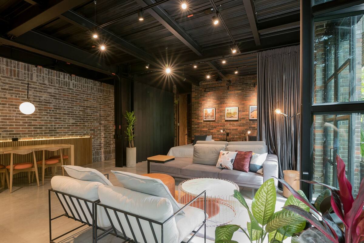 A modern living room with a brick wall, a sofa set, a dining table, and a large window.