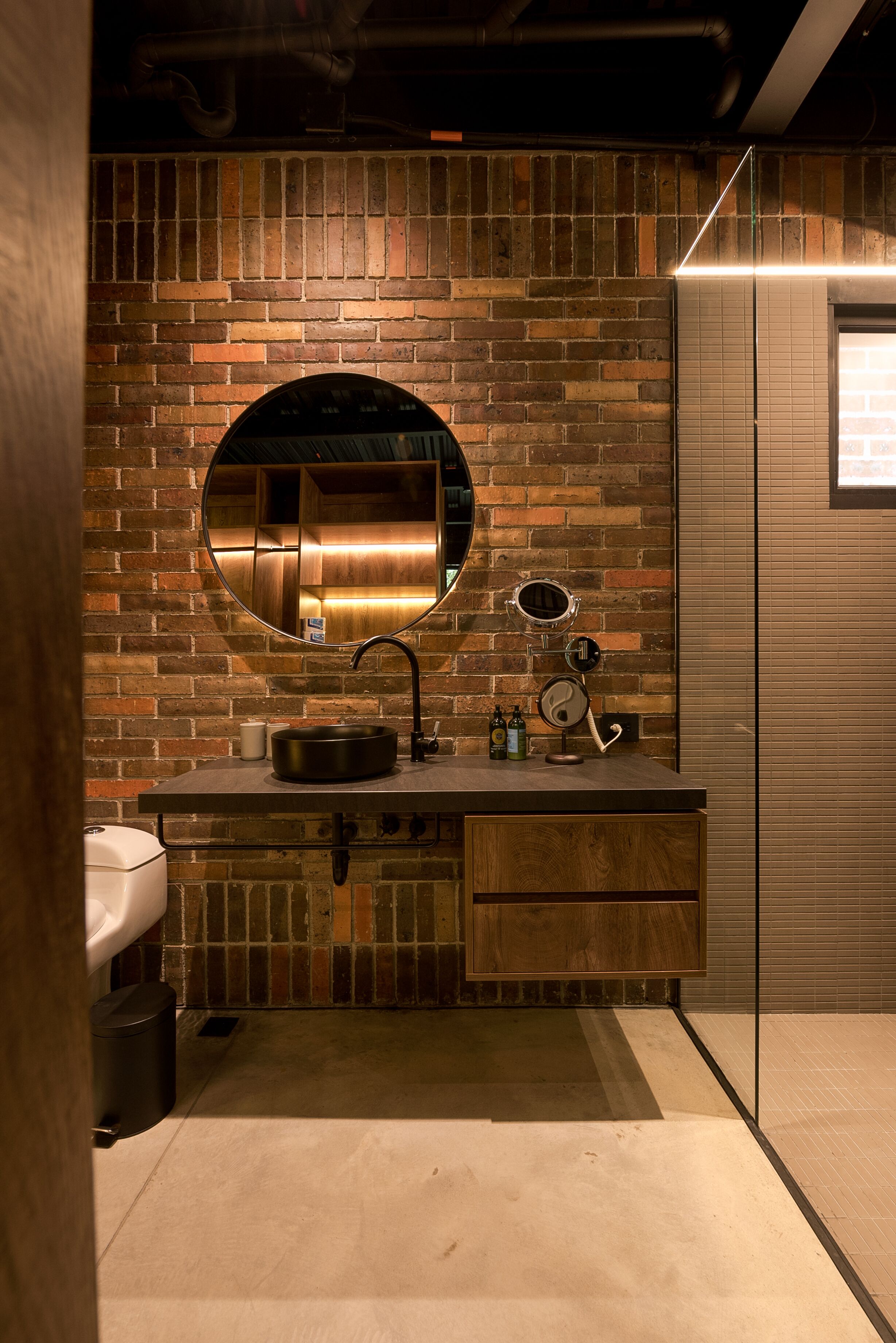 A bathroom with a brick wall, a round mirror, a sink, and a toilet.