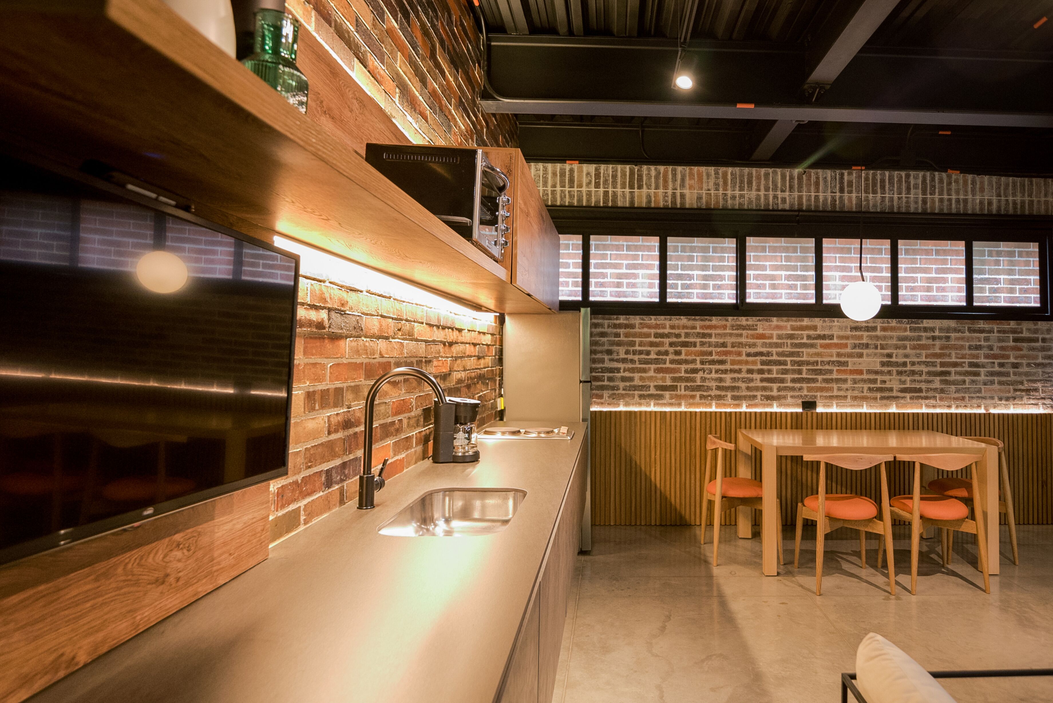 Cocina moderna con pared de ladrillo, electrodomésticos de acero inoxidable y zona de comedor de madera con sillas color naranja.