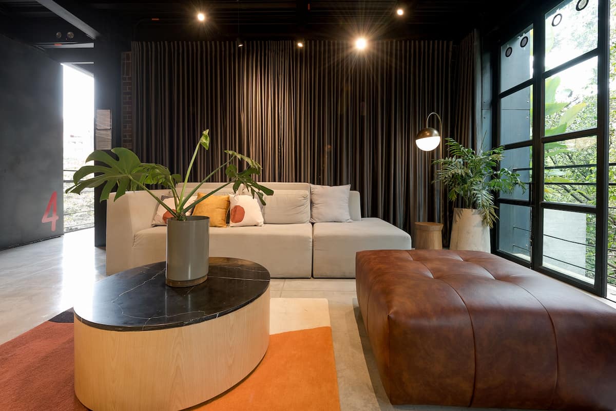 A modern living room with a sofa, a brown leather ottoman, a round coffee table, and potted plants.