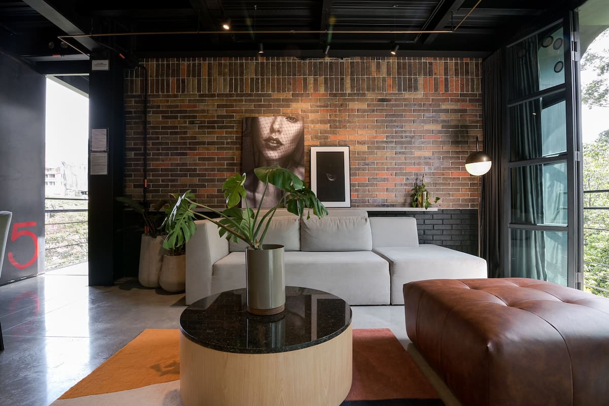 A modern living room with a brick wall, a large plant, a white sofa, and a leather ottoman.
