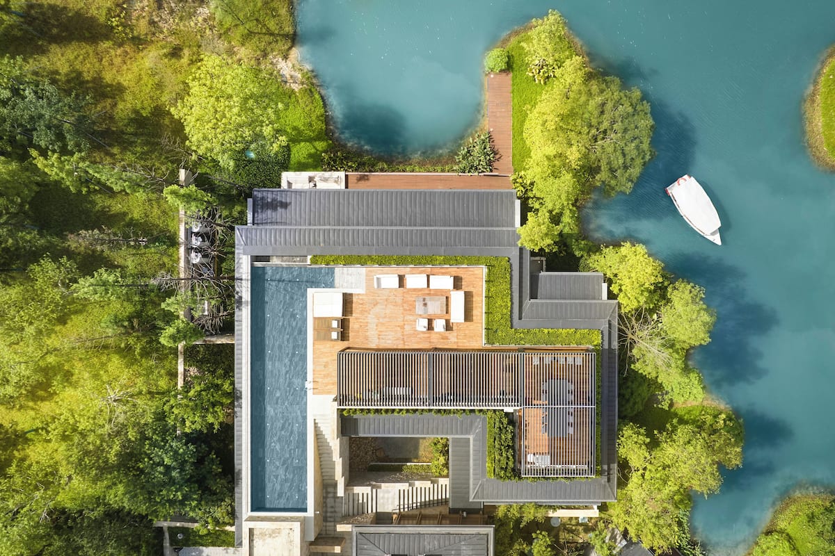 Ett flygbildsfoto av ett modernt hus med en swimmingpool, ett trädäck och en brygga för båtar.