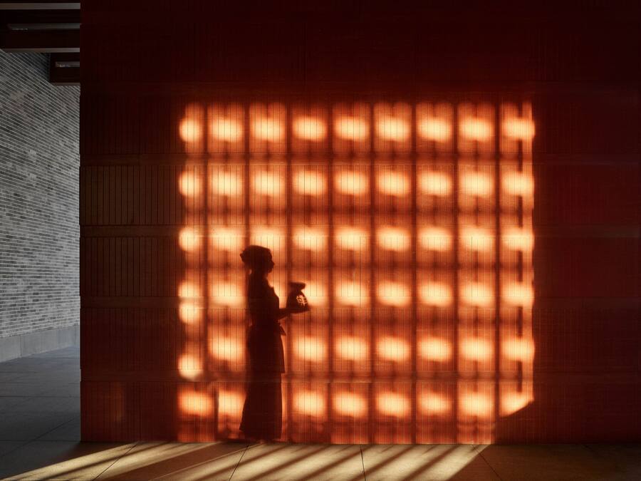 A person standing in front of a wall with a grid of lights, casting shadows on the floor.