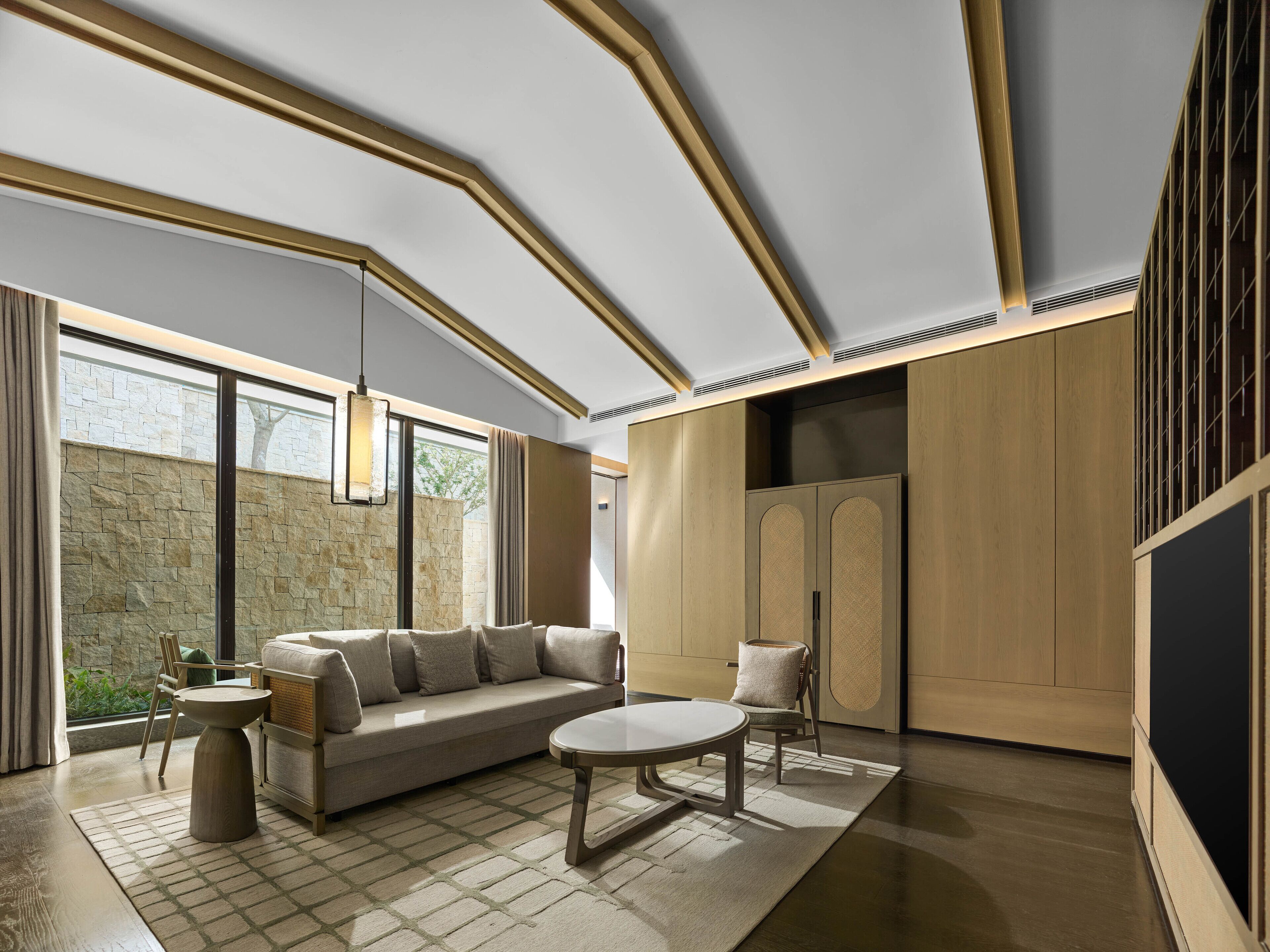 A modern living room with a sectional sofa, a round coffee table, and a stone wall.