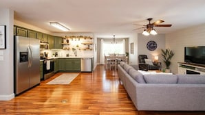 A modern kitchen with green cabinets, a stainless steel refrigerator, and a dining area with a sofa and TV. - Mountain Veiws, Hot Tub,Treehouse,Gameroom, Child playroom, pet friendly  (Verona)