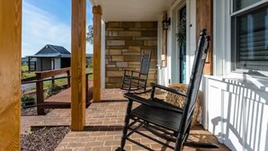 A covered porch with a stone wall, wooden columns, and two rocking chairs. - Luxury Farm Cottage, Hot Tub, Sauna,Massage,Shenandoah Views, pet friendly (Weyers Cave)