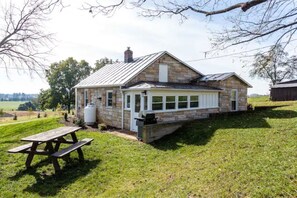A stone house with a covered porch, a picnic table, and a water tank in the yard. - Luxury Farm Cottage, Hot Tub, Sauna,Massage,Shenandoah Views, pet friendly (Weyers Cave)
