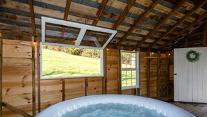 A wooden cabin with a hot tub, large windows, and a wreath on the door. - Luxury Farm Cottage, Hot Tub, Sauna,Massage,Shenandoah Views, pet friendly (Weyers Cave)