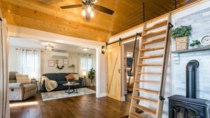 A spacious living area with wooden flooring, a ceiling fan, a black wood-burning stove, and a sliding barn door leading to another room. - Luxury Farm Cottage, Hot Tub, Sauna,Massage,Shenandoah Views, pet friendly (Weyers Cave)