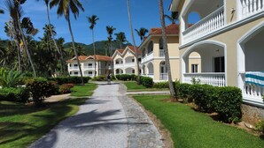 Un resort con edificios de varios pisos, un camino pavimentado y abundante vegetación, incluyendo palmeras.