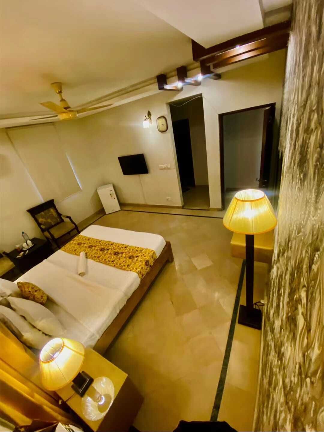 A hotel room with a bed, bedside tables, a lamp, a clock, and a television.