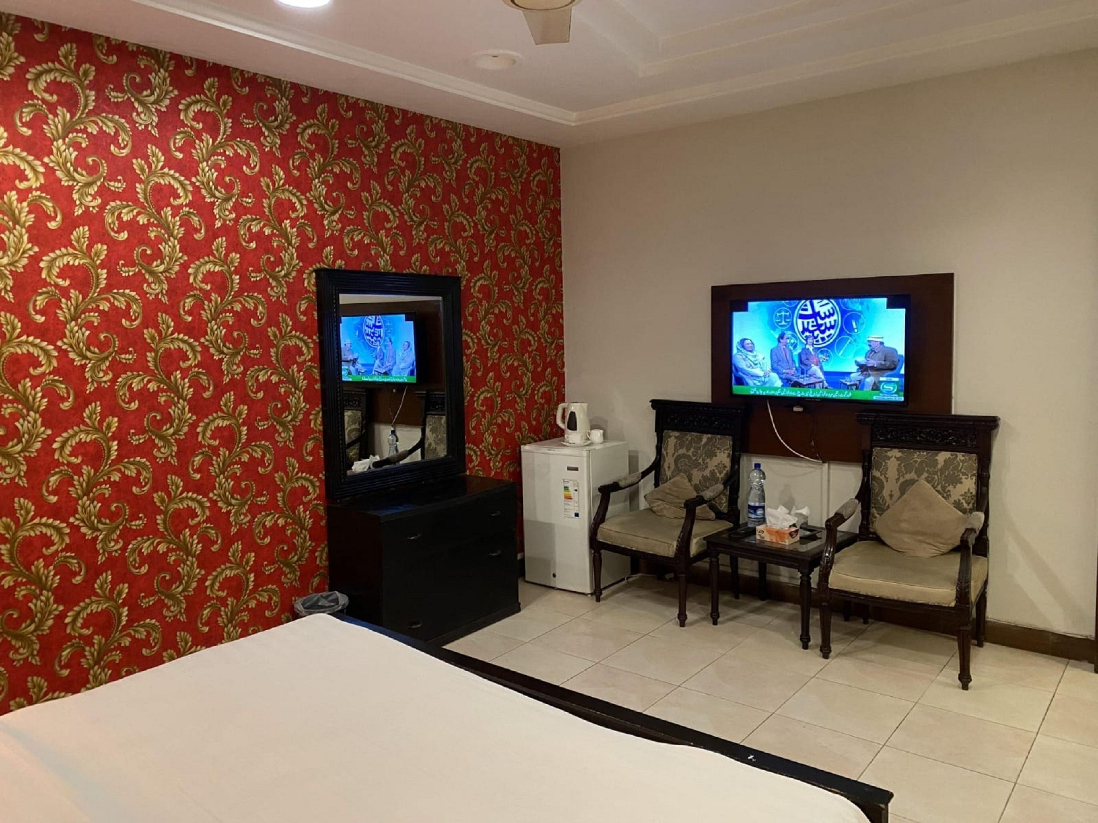 A hotel room with a bed, two armchairs, a TV, a small table, and a cabinet.