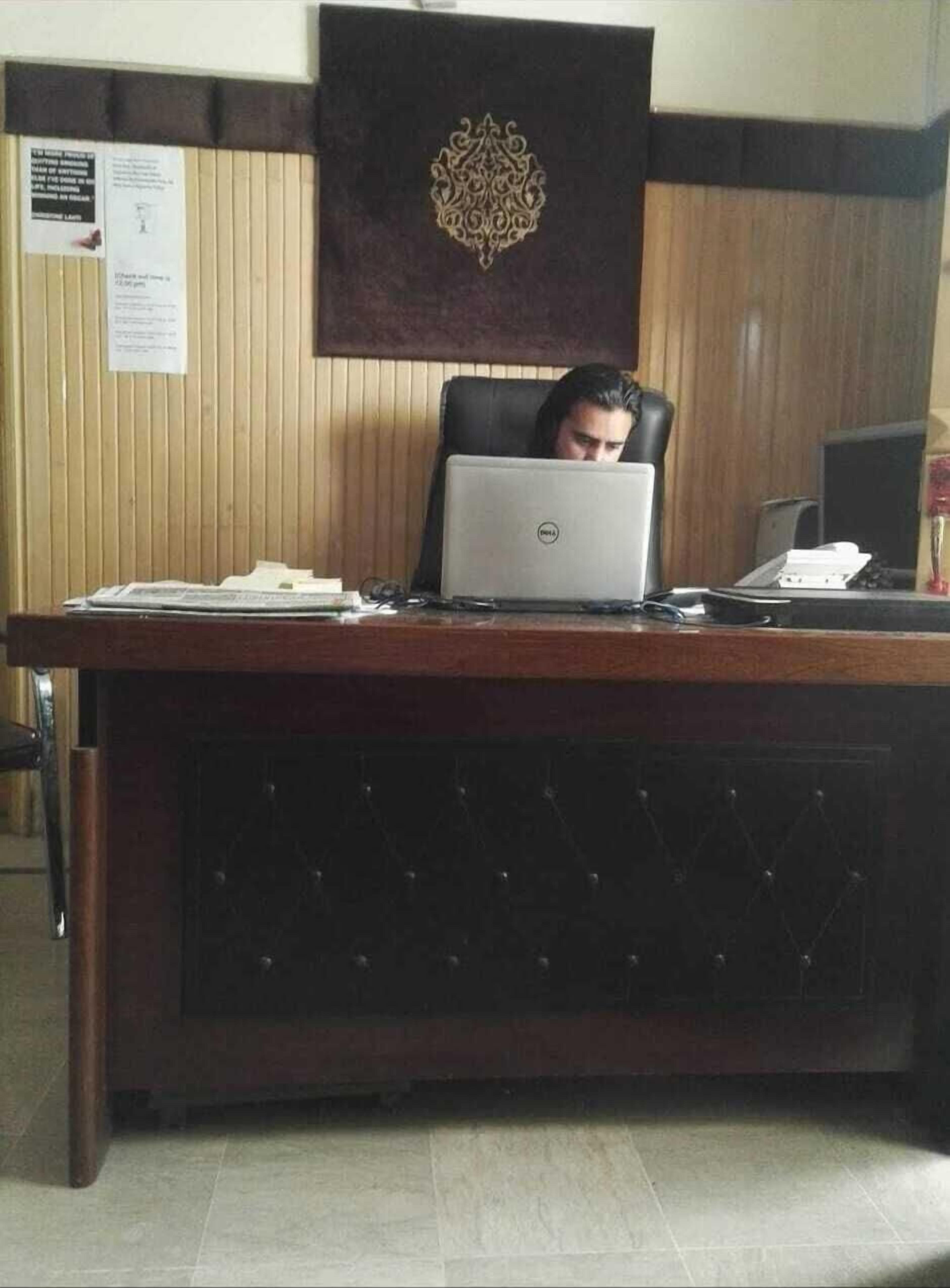 Un hombre sentado en un escritorio de madera con una computadora portátil, papeles y un teléfono.