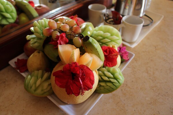 A fruit arrangement with a red flower centerpiece on a white plate.