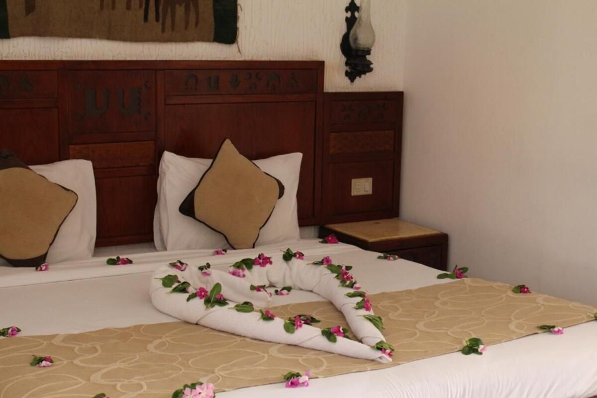 A neatly made bed with a patterned bedspread and decorative pillows, a wooden headboard, and a bedside table with a lamp.
