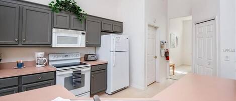 Une cuisine moderne avec des meubles gris, un réfrigérateur blanc, un four à micro-ondes, une cuisinière et un évier.