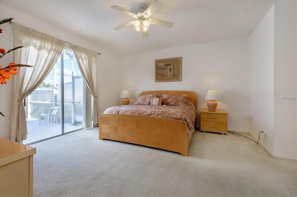 A bedroom with a bed, bedside lamps, a ceiling fan, a painting, and a sliding glass door to a balcony.