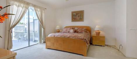 A bedroom with a bed, bedside lamps, a ceiling fan, a painting, and a sliding glass door to a balcony.