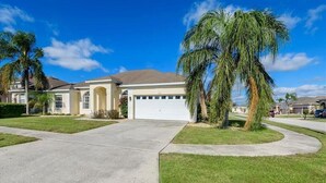 A residential house with a garage, palm trees, and a well-maintained lawn. - Private Pool Villa Near Disney with Golf, Patio & Resort Amenities (Davenport)