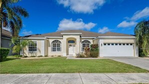 A two-story house with a front garage, a central entrance with a door, and a well-maintained lawn. - Private Pool Villa Near Disney with Golf, Patio & Resort Amenities (Davenport)