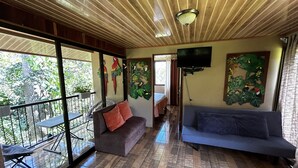 A spacious living area with a balcony, a sofa, a couch, and a TV mounted on the wall.