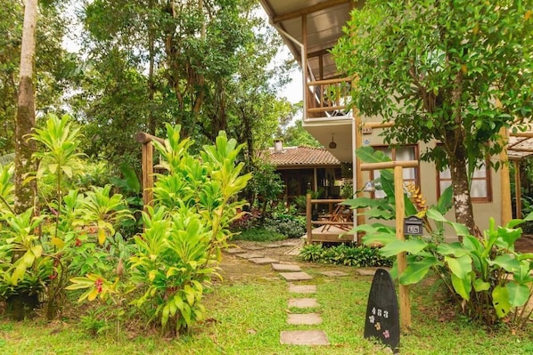 A bungalow with a thatched roof, surrounded by lush greenery and a stone pathway.