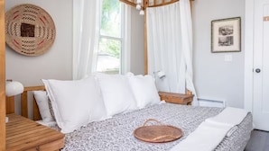 Une chambre à coucher avec un lit à baldaquin en bois, du linge de lit blanc, un panier en osier et un tableau encadré au mur.