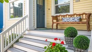 Un porche à l’avant de la maison, avec un banc, des marches et des plantes en pot.