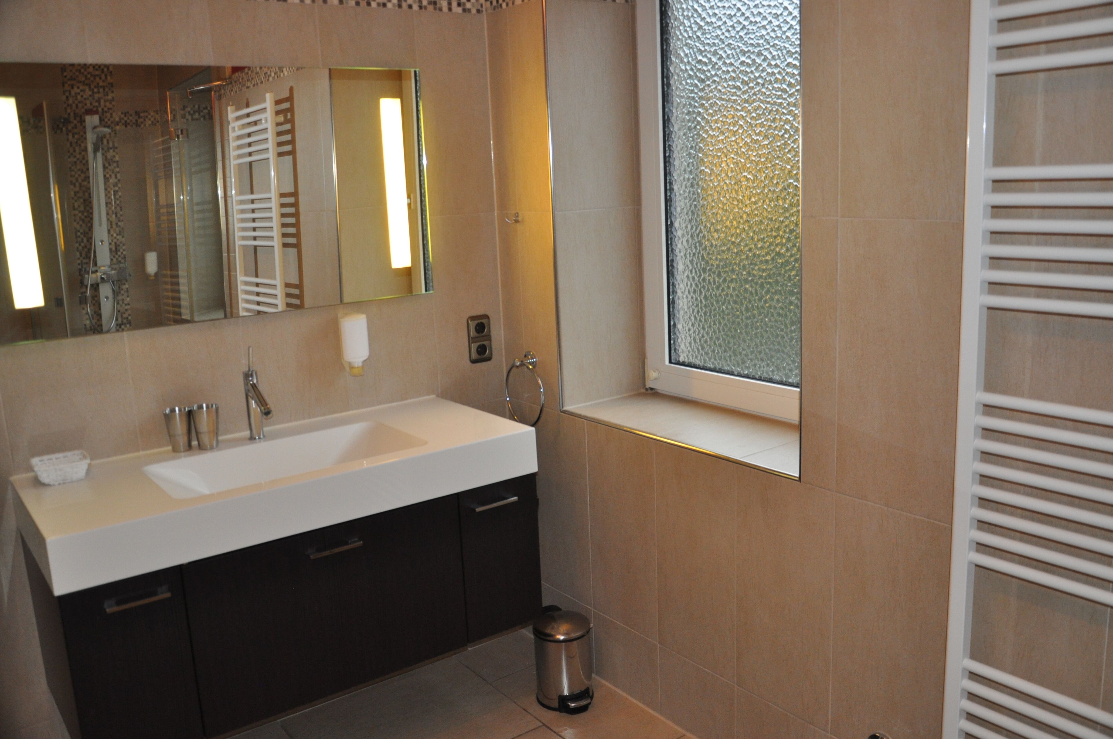 A modern bathroom with a large mirror, a sink, and a window.