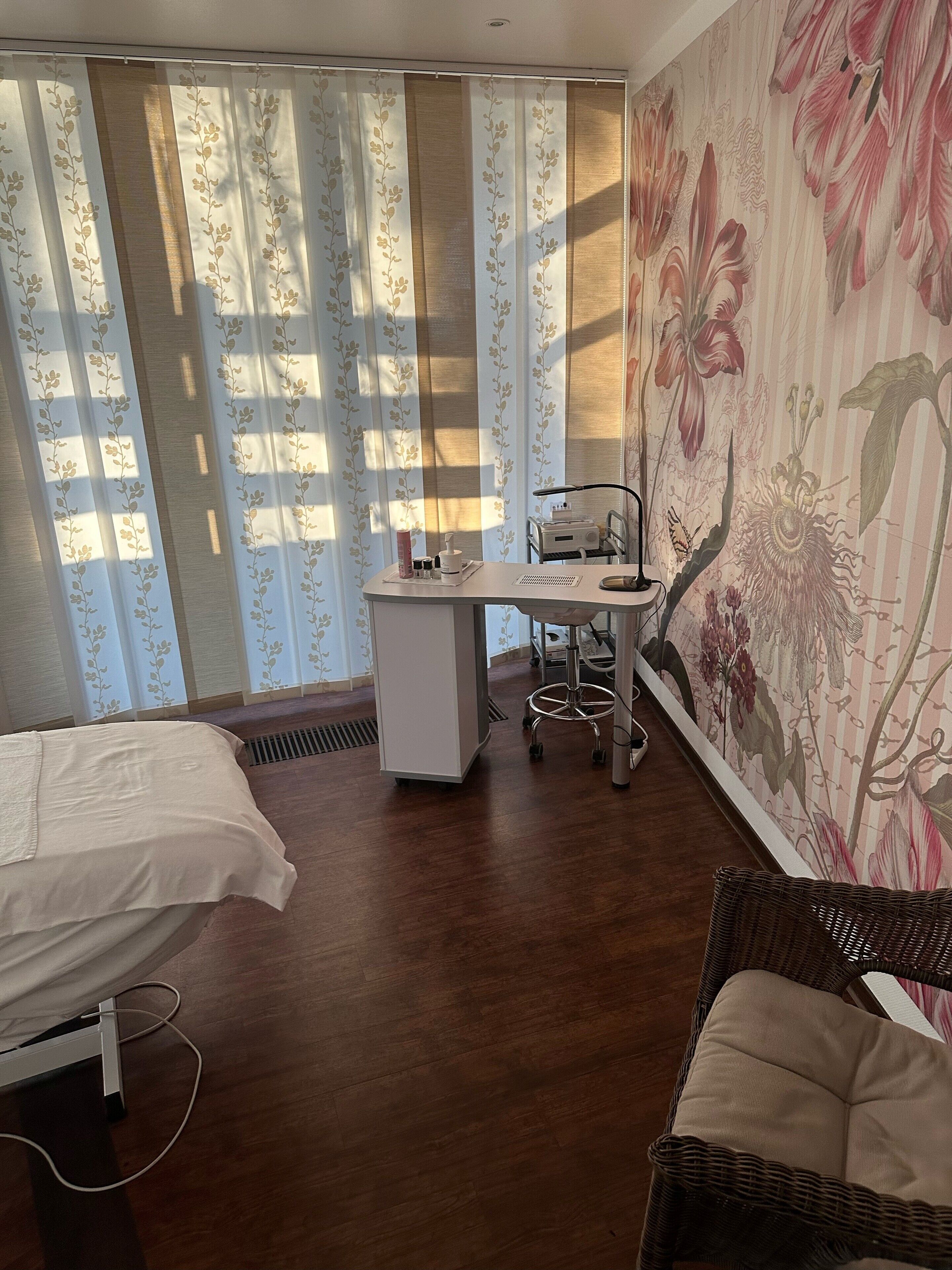 Una stanza con un letto, una scrivania con una sedia, una sedia in vimini e una parete con carta da parati a motivi floreali.