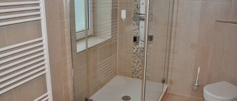 Un baño con ducha de vidrio, inodoro y ventana.