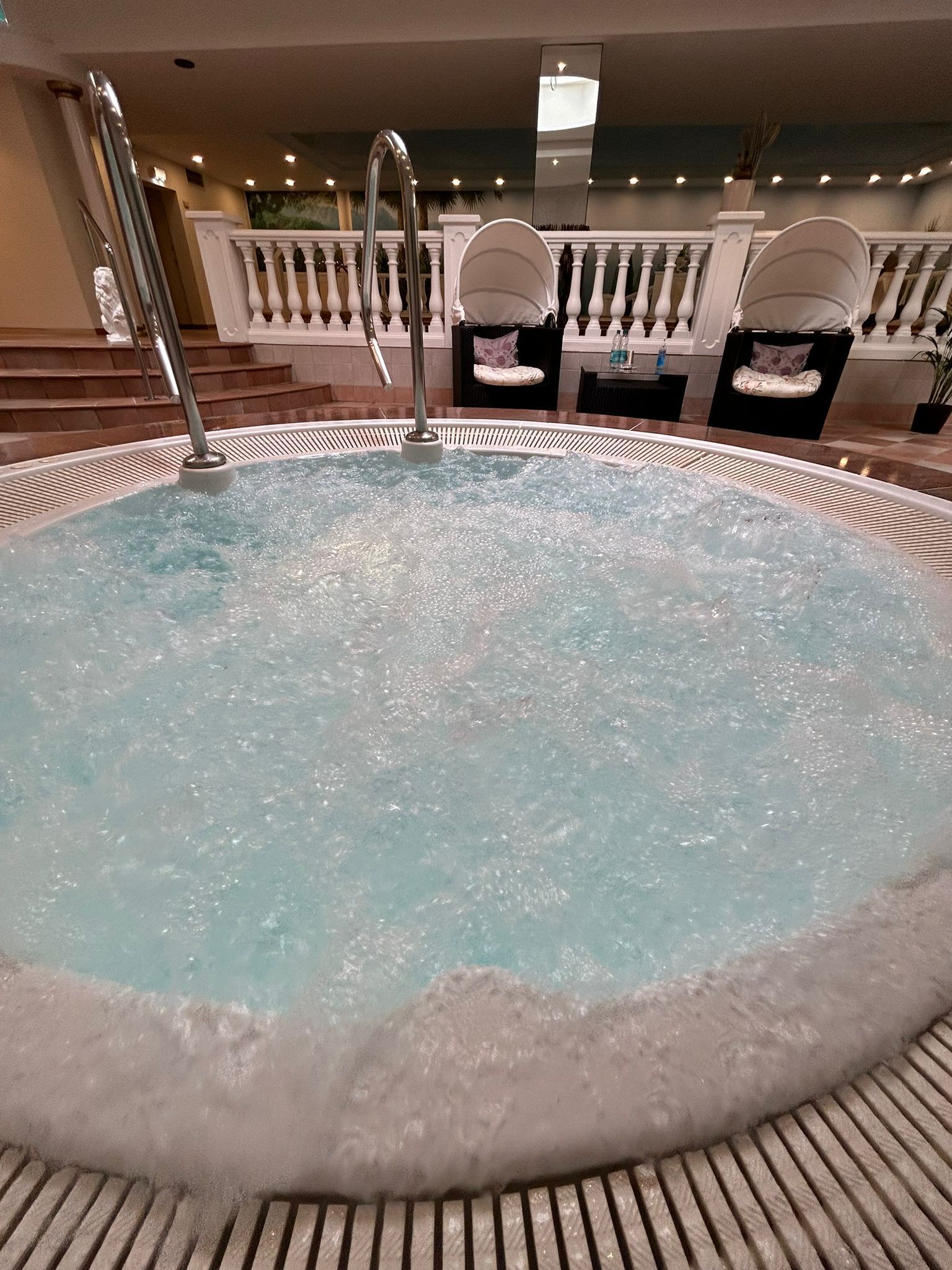 A hot tub with a metal ladder, surrounded by a white railing and a few chairs.