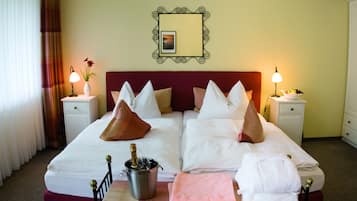 A hotel room with a large bed, two bedside tables, a bedside lamp, a mirror, and a bottle of champagne.