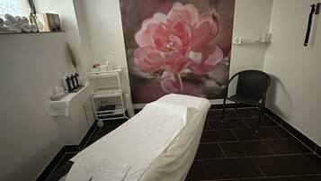 A clinical room with a single bed, a chair, a shelf with toiletries, and a large floral mural on the wall.