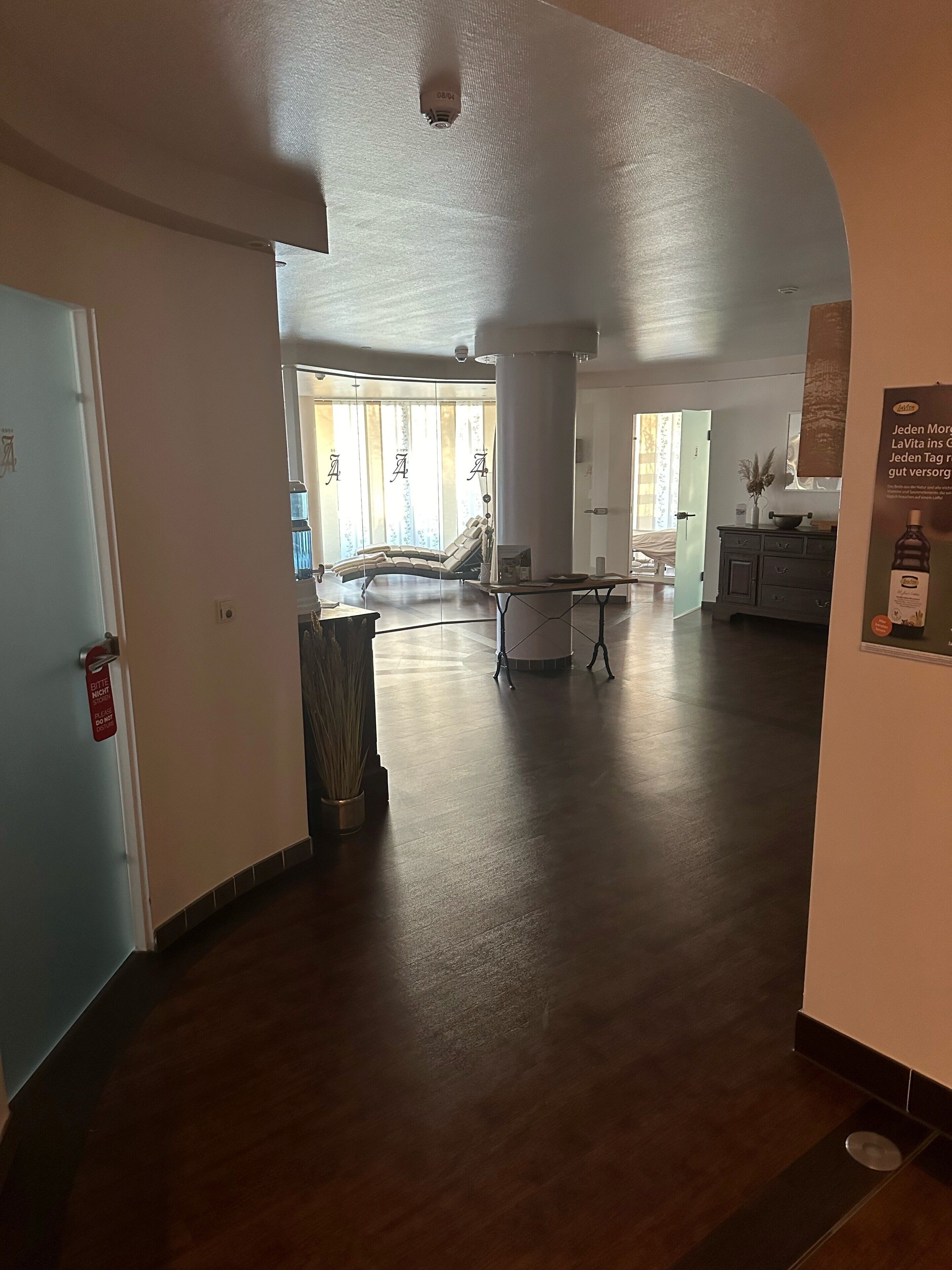 A hotel lobby with a wooden floor, a seating area with a sofa and chairs, a trash bin, and a sign on the wall.