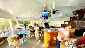 A spacious outdoor area with a ping pong table, a wooden bar, and a television mounted on the ceiling.