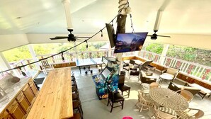 A covered outdoor dining area with multiple tables and chairs, a large screen, and a ceiling fan.