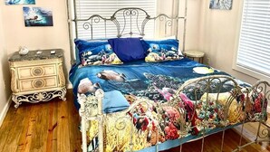 A bedroom with a metal bed frame, a blue and yellow patterned bedspread, and a small bedside table with a lamp.