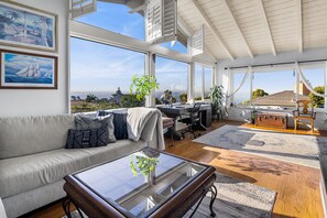 Ein großzügiger Wohnbereich mit einem großen Fenster und Blick auf eine reizvolle Landschaft, einem bequemen Sofa, einem Glastisch und einem Schreibtisch mit Globus.