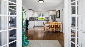 A modern kitchen with white cabinetry, a wooden dining table, and a view of the outdoors. - Ocean View, Gym, Sauna, Garden, and Private Beach! (Laguna Beach)