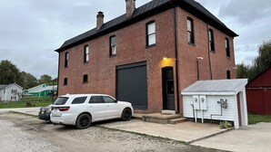 A two-story brick house with a garage door, a small shed, and a white SUV parked in front. - Vaudeville Suite, Romantic King Stay Just 4 Min from Hermann Wineries (Hermann)