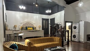 A modern living room with a sofa, a coffee table, a bed with a headboard, a staircase, and a washing machine. - Vaudeville Suite, Romantic King Stay Just 4 Min from Hermann Wineries (Hermann)