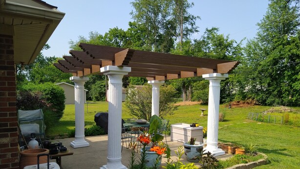A covered patio area with white columns, a pergola, outdoor furniture, and a garden with flowers and plants.
