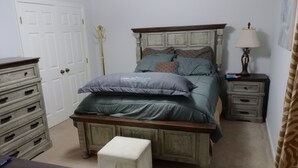 A bedroom with a bed, a nightstand, a dresser, and a door.