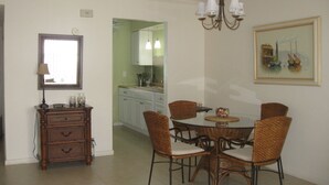 A dining area with a round table and six wicker chairs, a wooden cabinet with drawers, a chandelier, a framed painting, and a view into the kitchen. - LOVELY APARTMENT 1 MILE TO BEACH - DEERFIELD BEACH - FREE PARKING (Deerfield Beach)