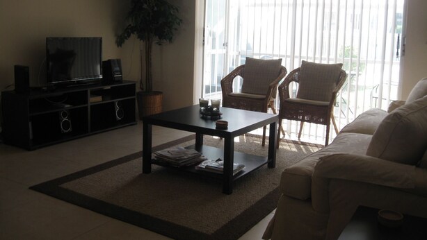 A living room with a TV, a coffee table, two wicker chairs, a sofa, and a large window with blinds. - LOVELY APARTMENT 1 MILE TO BEACH - DEERFIELD BEACH - FREE PARKING (Deerfield Beach)