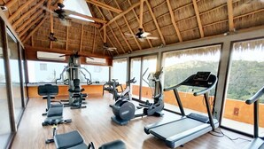 Une salle de sport équipée de tapis de course, d’appareils de musculation et d’un ventilateur au plafond.