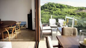 Une chambre moderne comprenant un coin repas, un canapé et un balcon offrant une vue sur une colline boisée.
