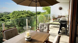 Un balcon avec une table, des chaises, un parasol et une vue sur un paysage luxuriant.
