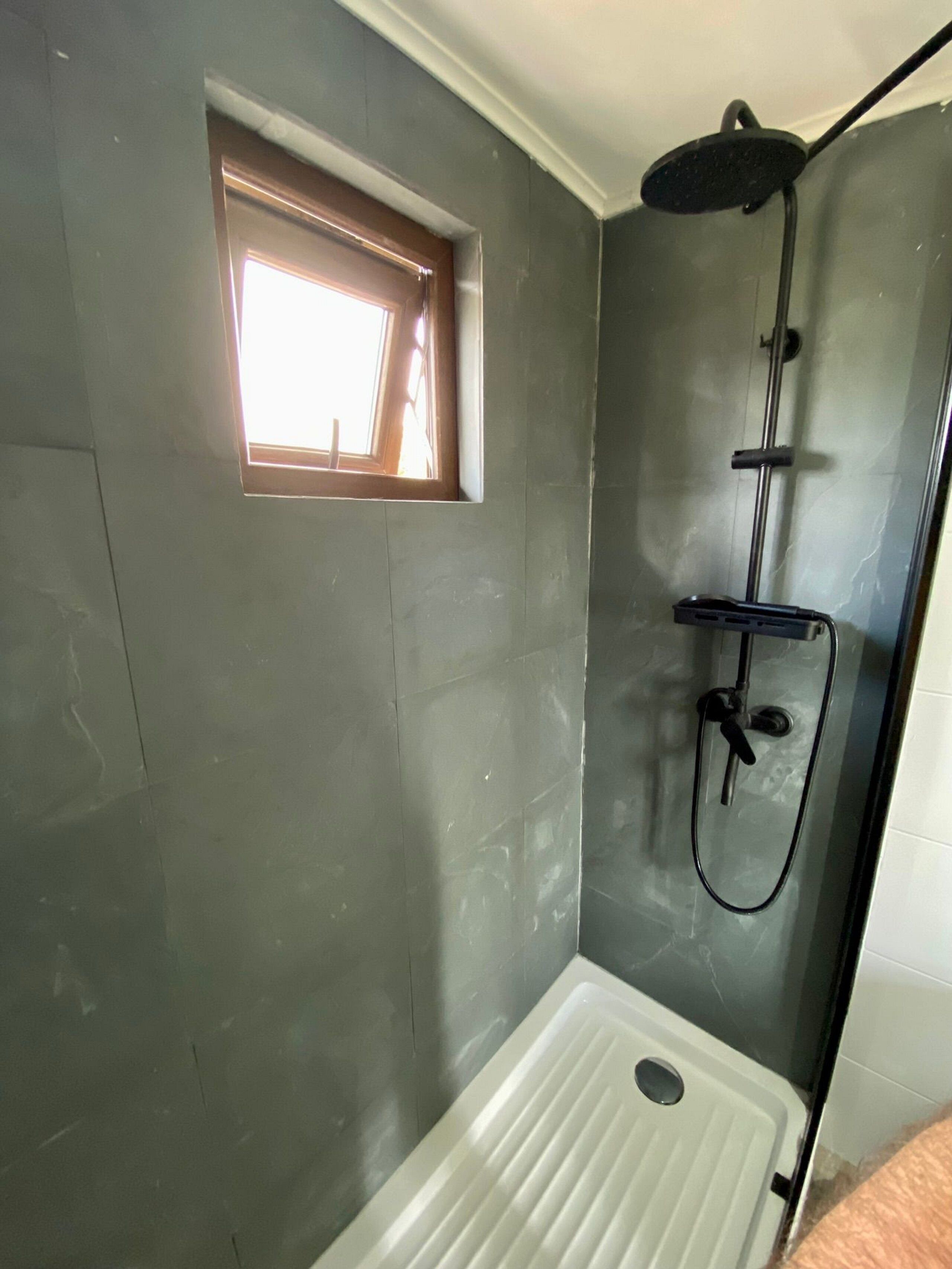 A shower area with a window, a showerhead, and a white sink.